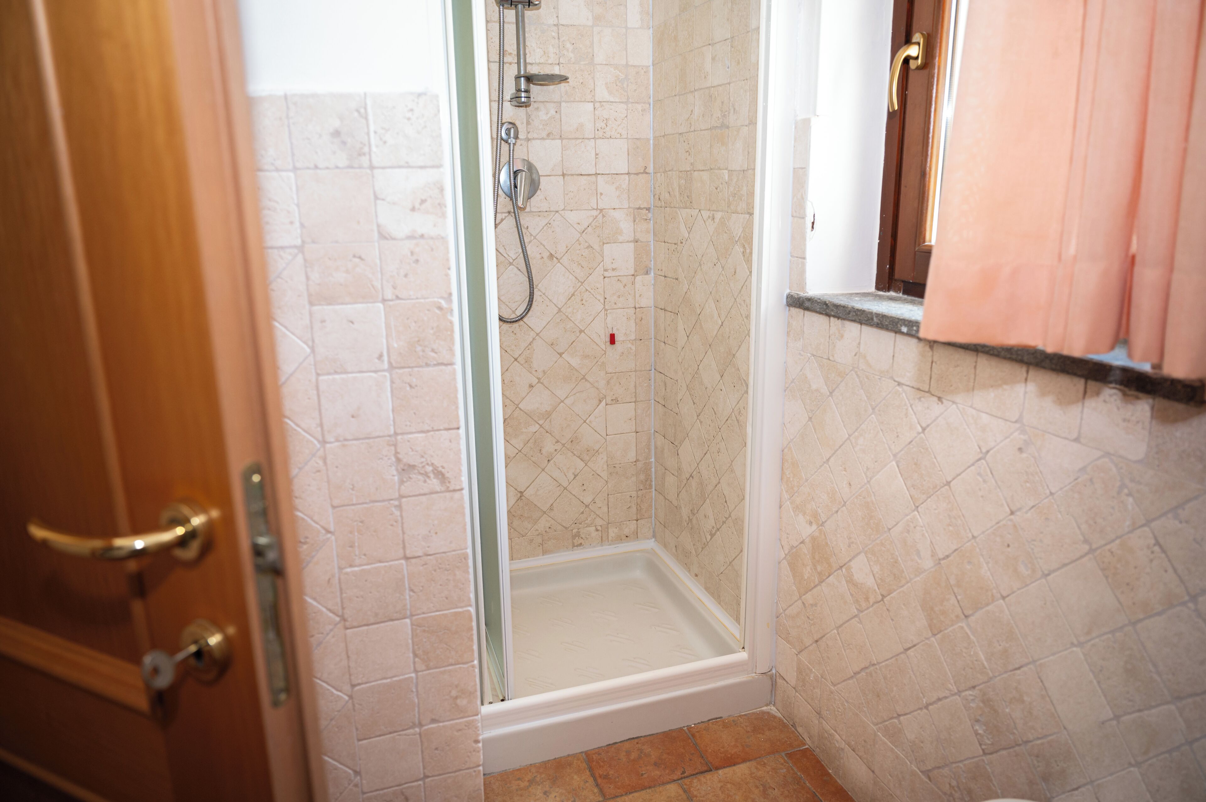 A shower with a glass door, tiled walls, and a wooden door with a brass handle.