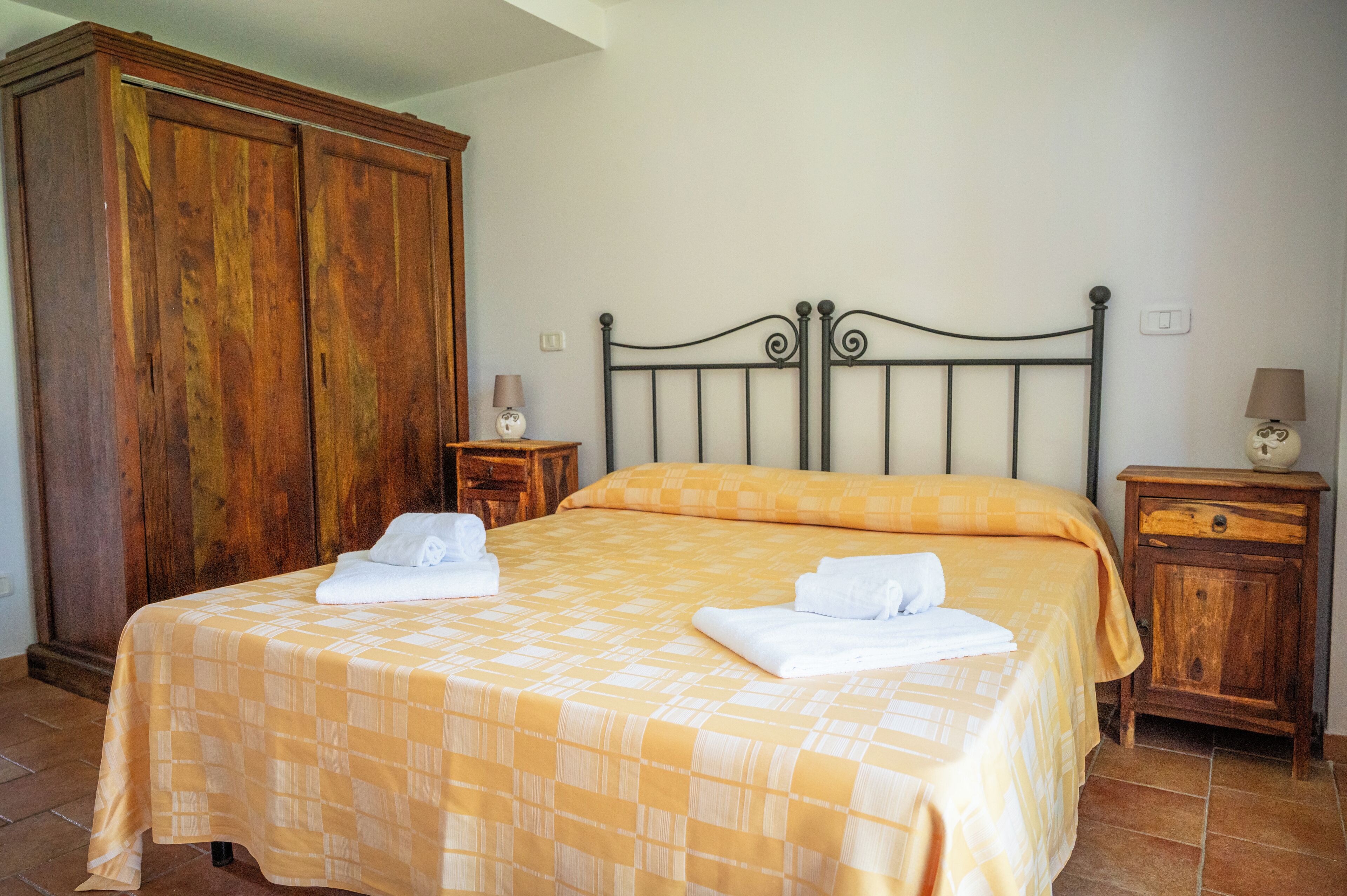 Une chambre à coucher avec un lit, une armoire en bois, des tables de chevet et une lampe.
