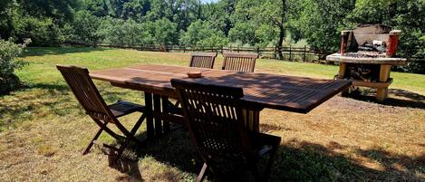 Un juego de mesa y sillas de madera al aire libre, con una parrilla de piedra en el fondo.