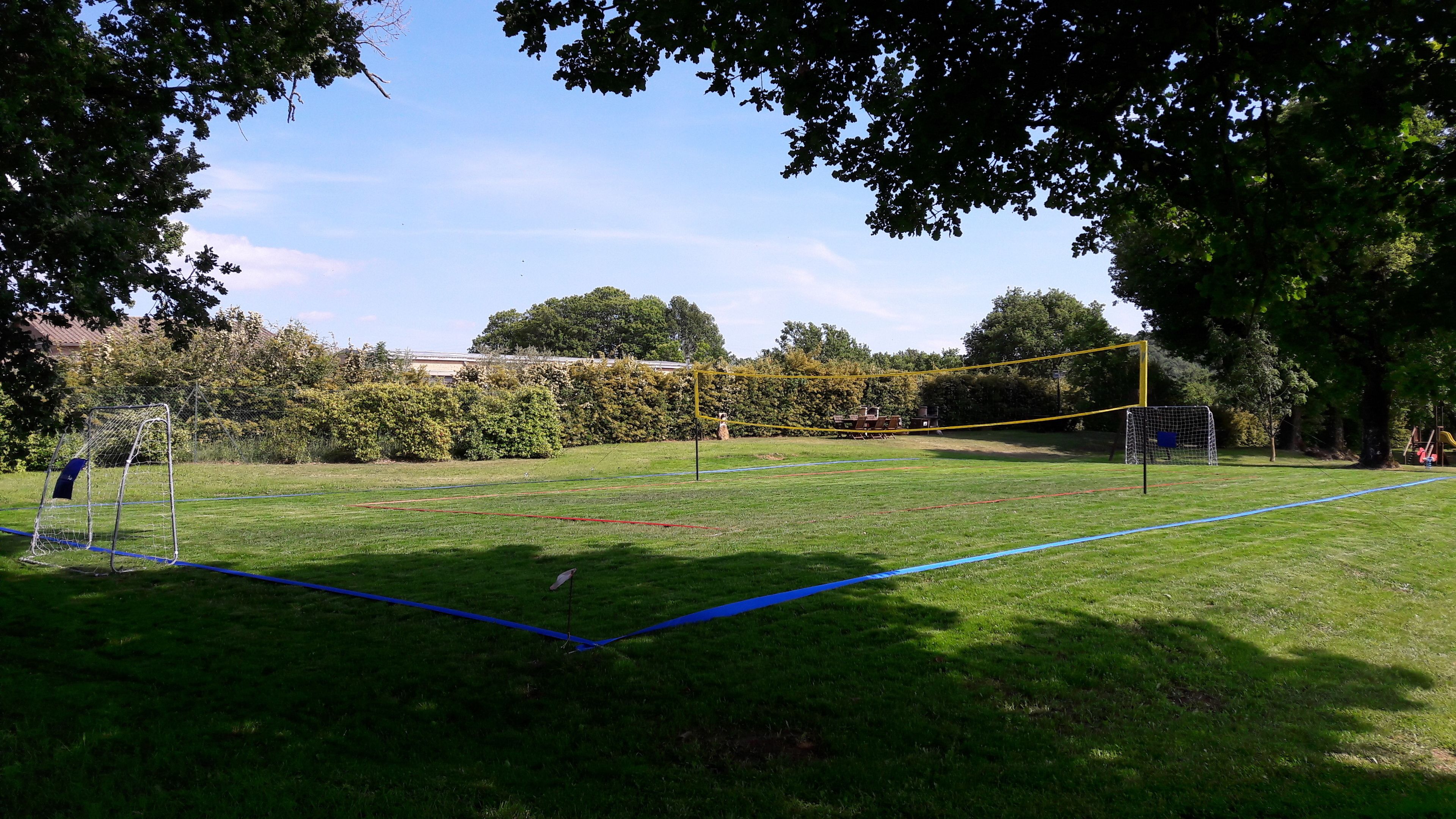 A grassy field with two soccer goals and a yellow net in the center.