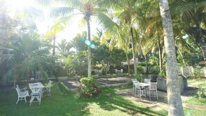 A garden with palm trees, a patio with white metal chairs, and a small table. - Residence Villas Mont Choisy (Mont Choisy)