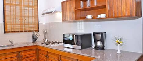 Una cocina con armarios de madera, un microondas, una cafetera y un ventanal con persianas.