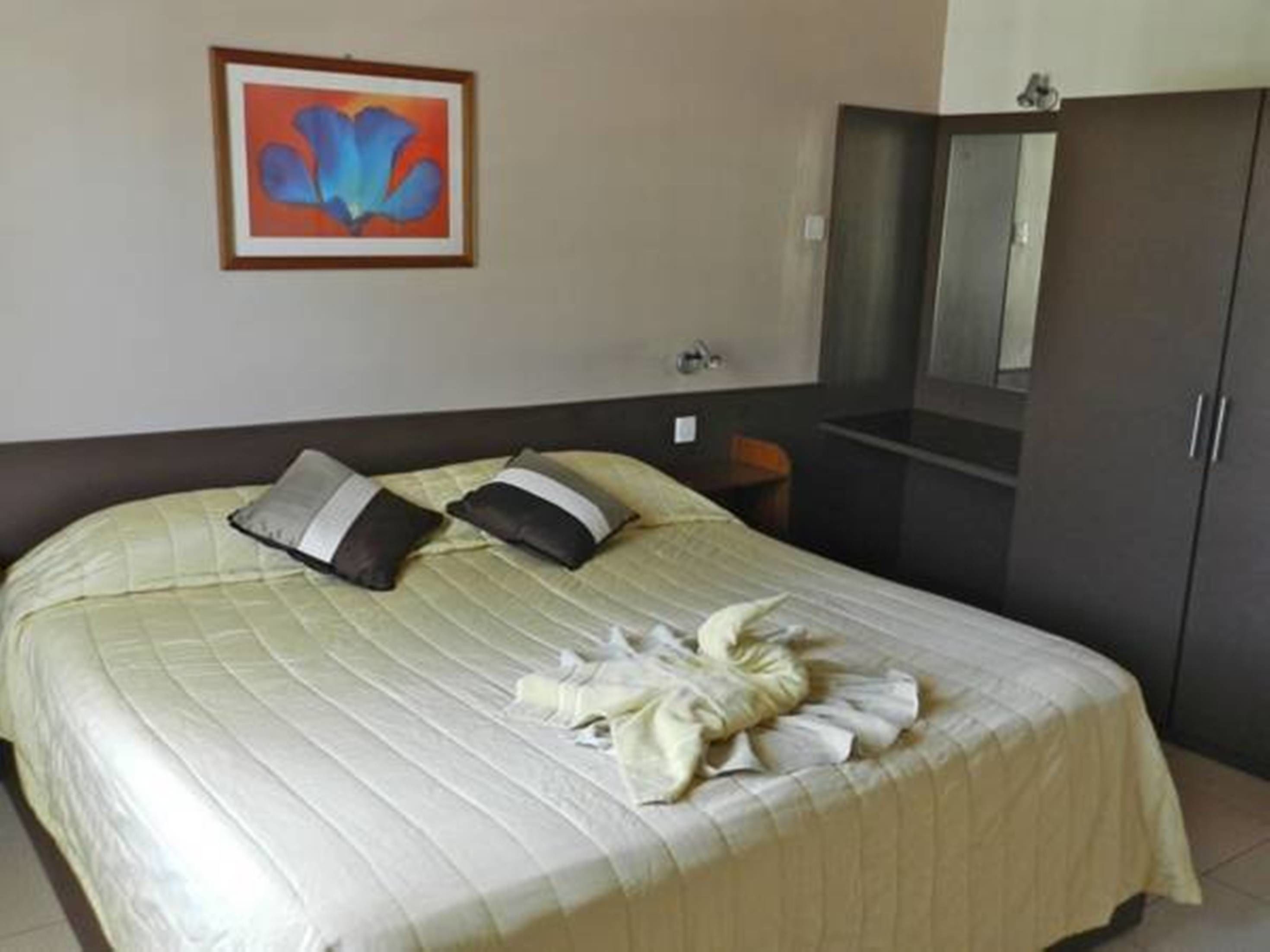 A hotel room with a bed, pillows, a towel, a mirror, and a wardrobe.