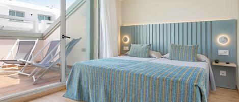 A bedroom with a bed, a nightstand, a wall-mounted light, a window with a curtain, and a balcony with chairs.