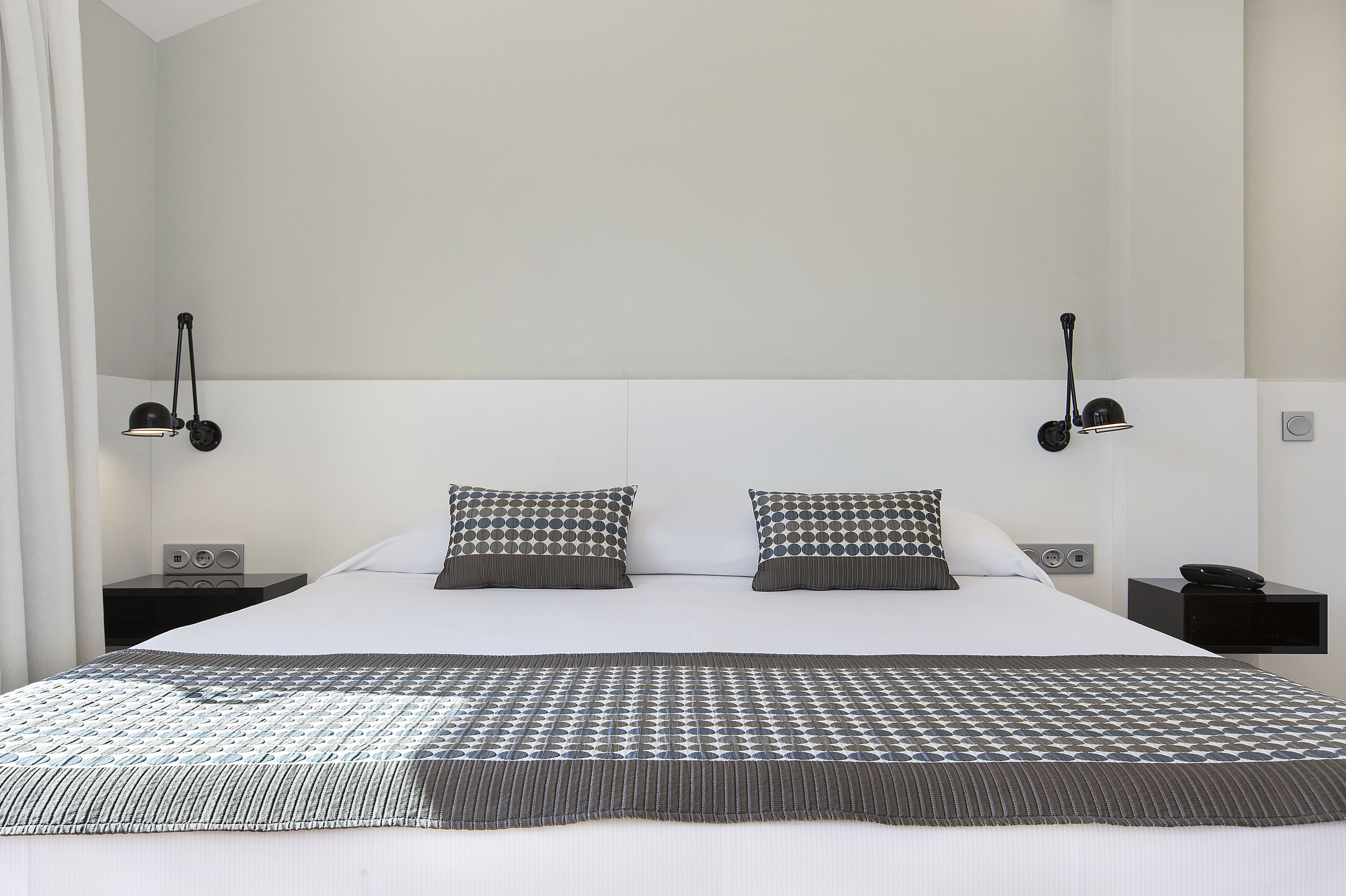 A hotel room with a large bed, two bedside tables, and two wall-mounted lamps.