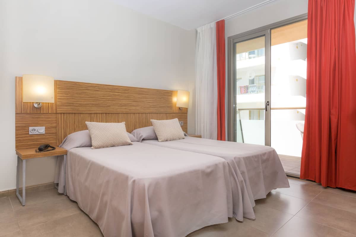 Hotelkamer met twee bedden, een houten hoofdbord, bedlampen, een nachtkastje en uitzicht op het balkon.