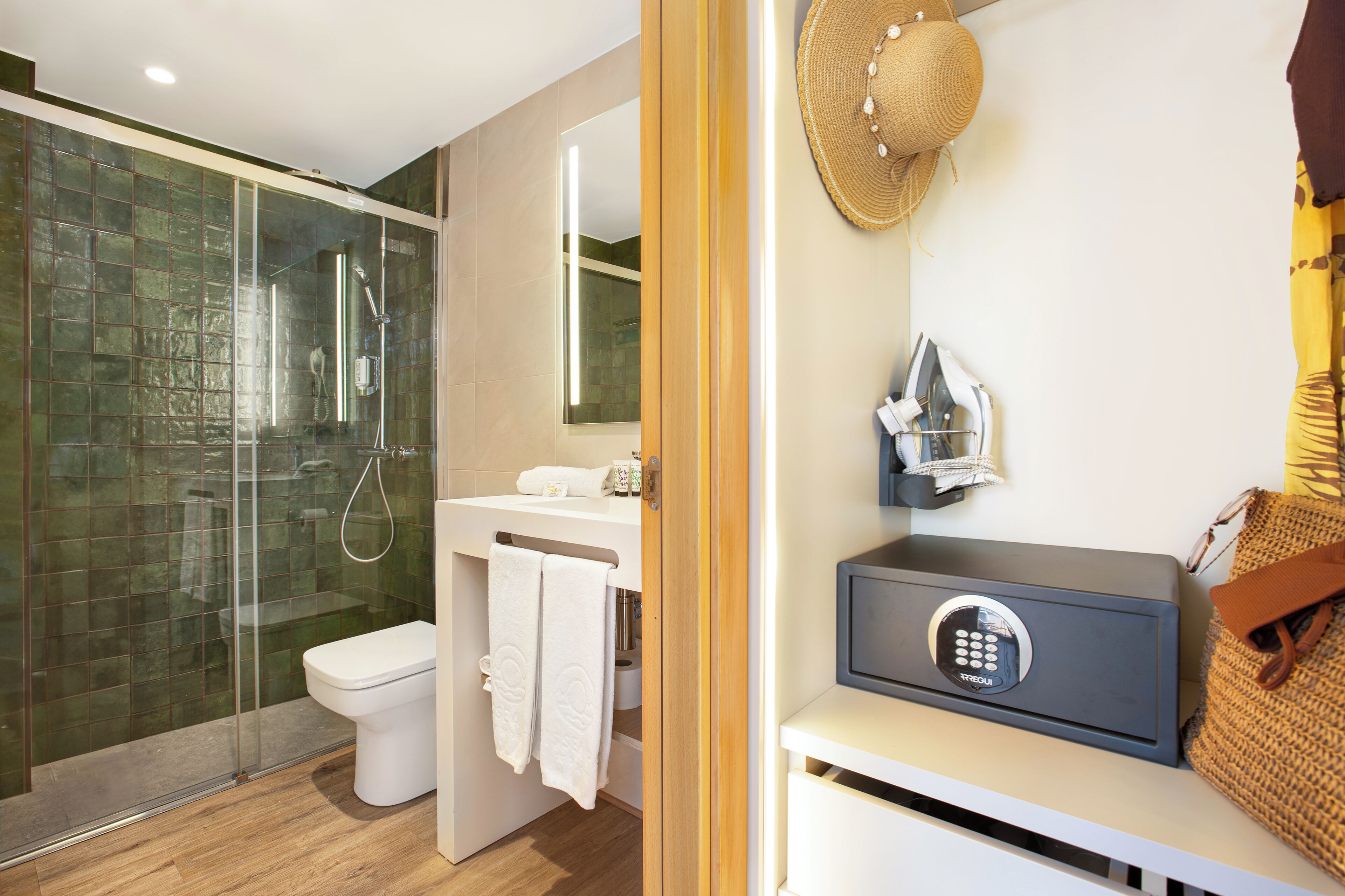 A modern bathroom with a glass shower enclosure, a toilet, a sink with a towel rack, and a security device on the counter.