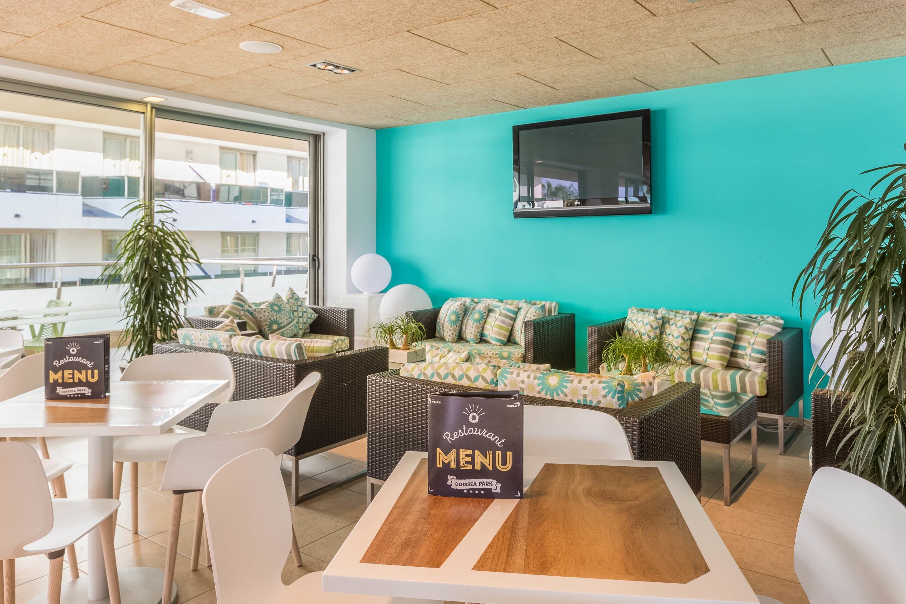 A restaurant with a teal wall, wicker furniture, and a menu stand.