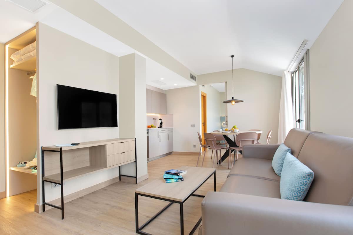 Een moderne woonkamer met een flatscreen-tv, een bank, een salontafel en een eethoek met een tafel en stoelen.