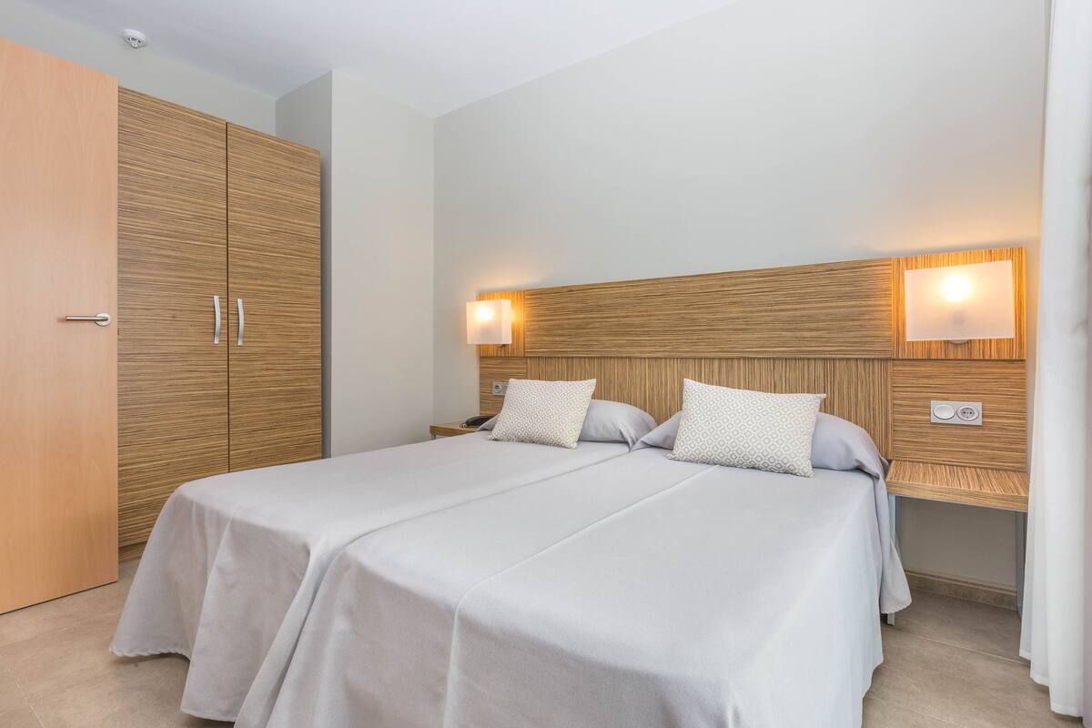 Een tweepersoonsbed met houten hoofdeinde, twee nachtkastjes en een wandlamp.