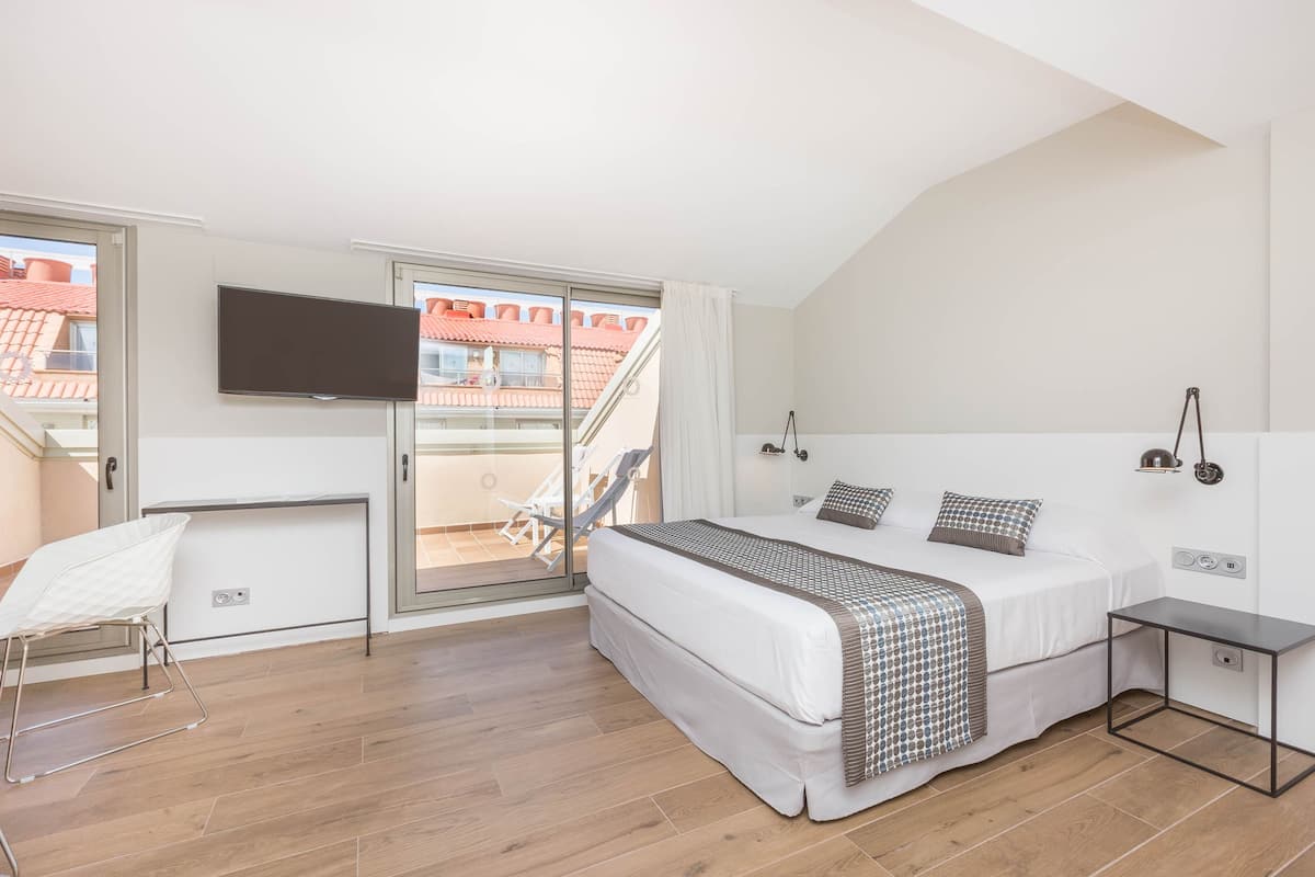 Een slaapkamer met een bed, een televisie, een stoel en een balkon met uitzicht op gebouwen.