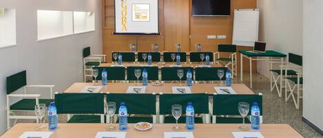 A conference room with multiple tables, chairs, water bottles, and a presentation screen.