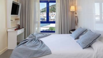 Habitación de hotel con cama, televisión en una estantería, escritorio y vistas a edificios a través de una ventana.