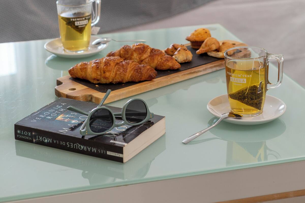A neatly arranged breakfast table with croissants, a cup of tea, and a book.
