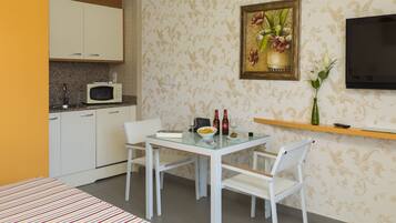 Una habitación compacta con kitchenette, una mesa de comedor con sillas, una cama y un televisor montado en la pared.
