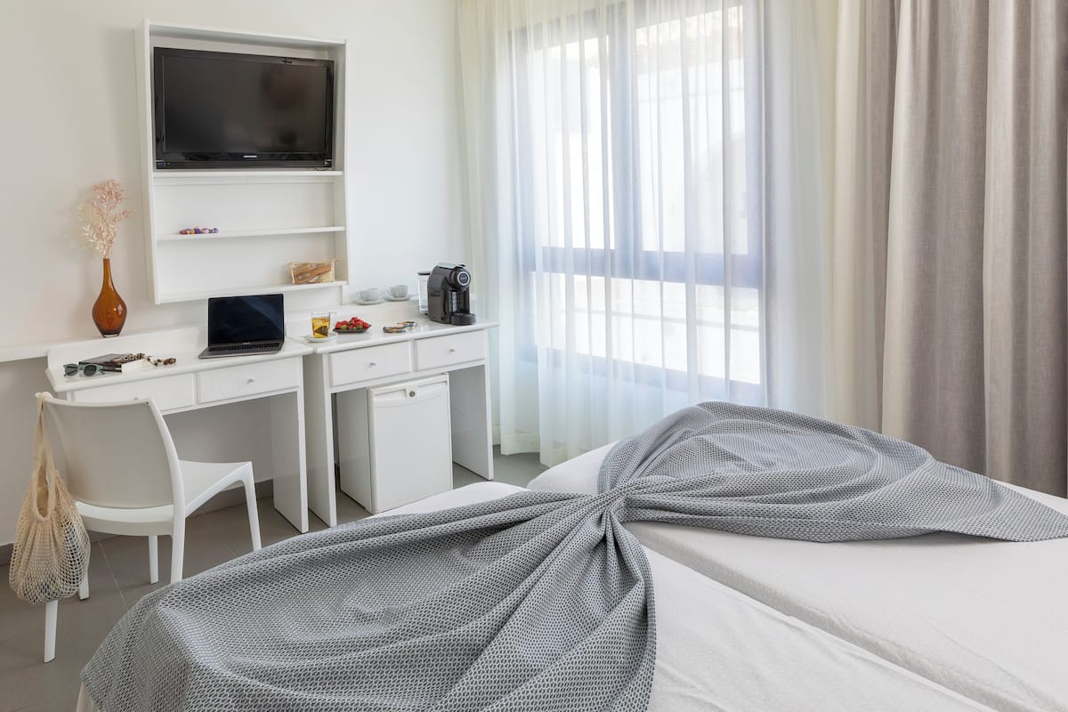 A hotel room with a bed, a desk with a laptop, a coffee maker, and a TV.