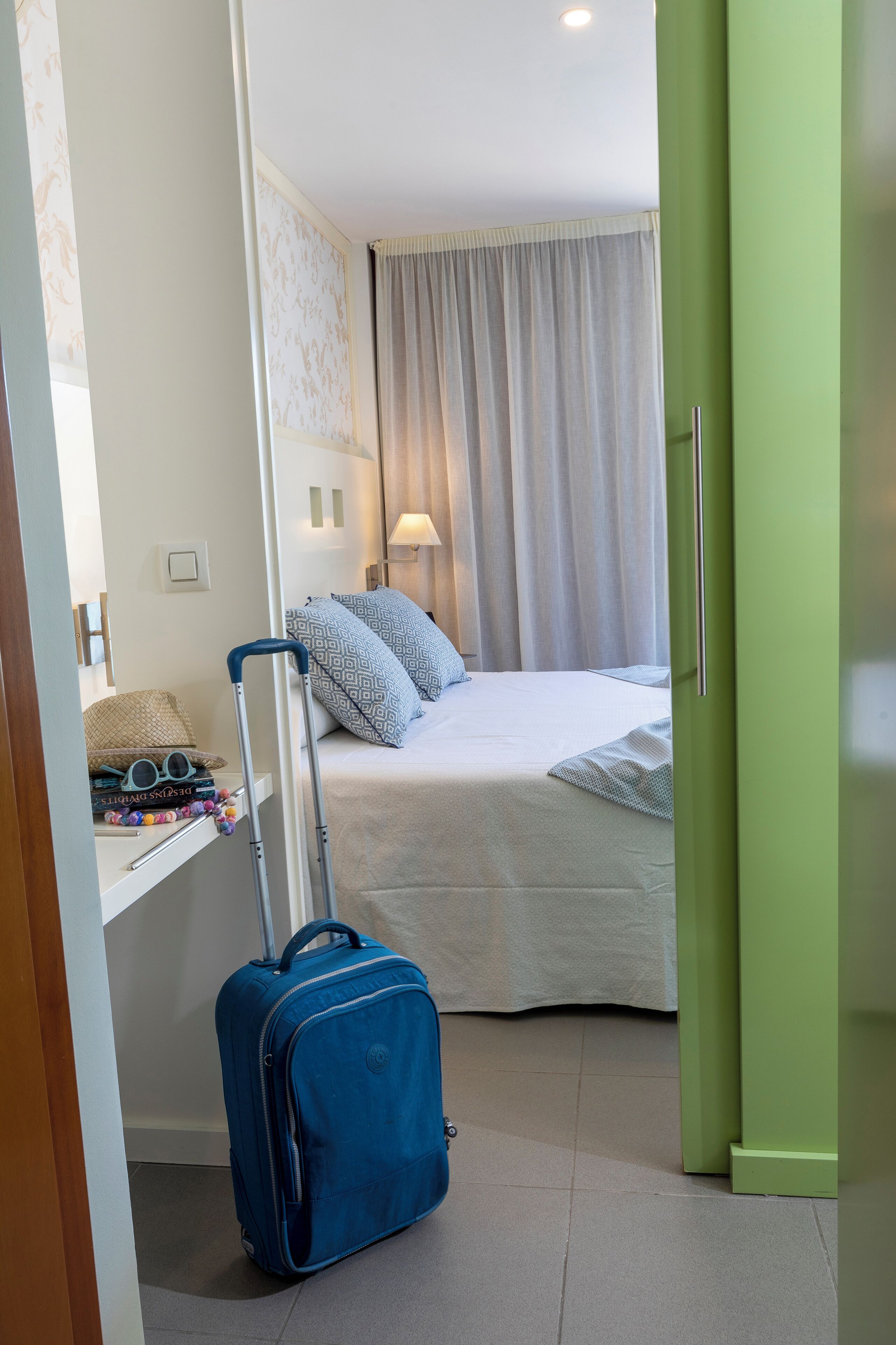 Una habitación de hotel con cama, maleta y mesita de noche con lámpara.