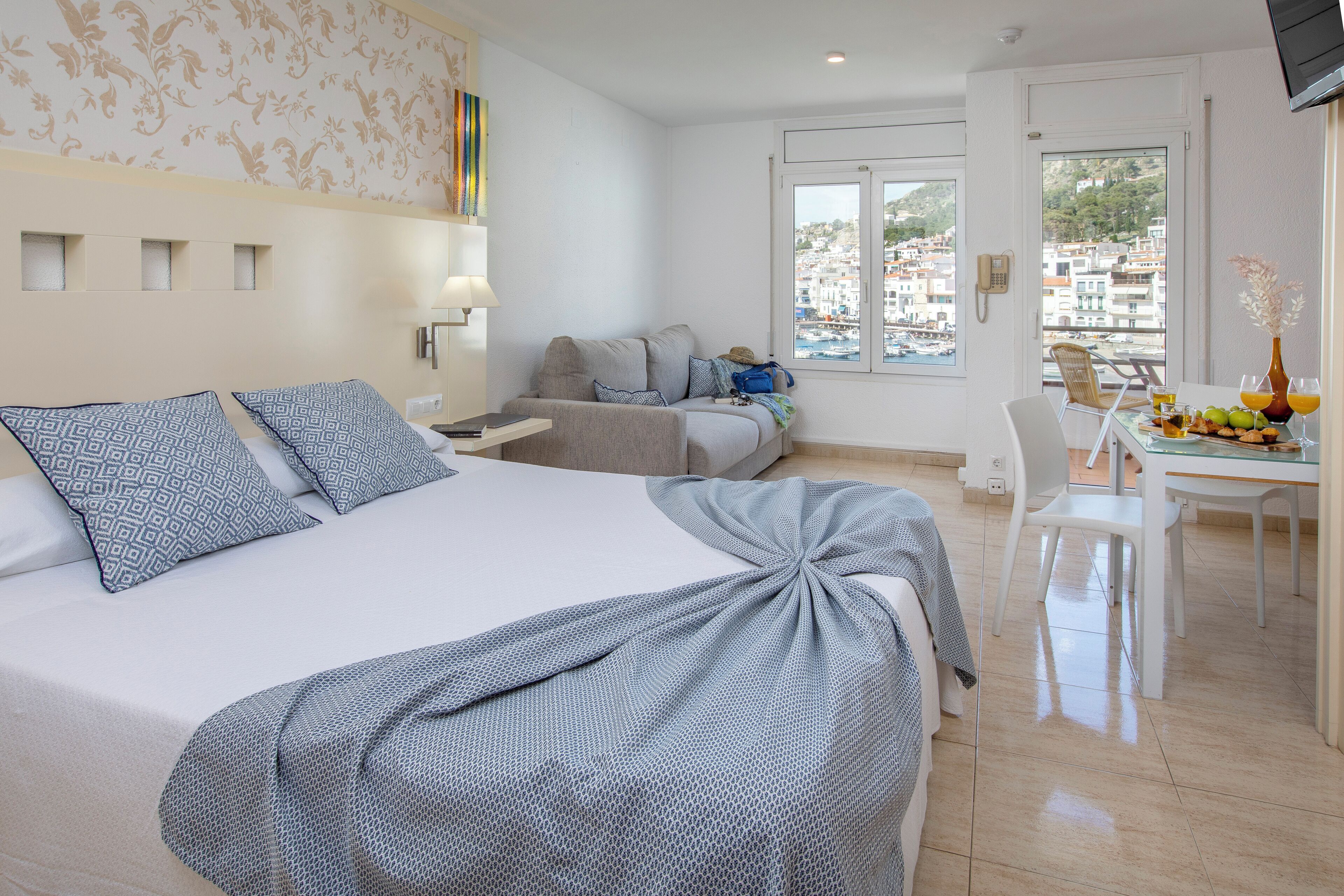 Habitación de hotel con una cama grande, un escritorio con silla, una mesa de comedor con sillas y vistas a la ciudad a través del ventanal.
