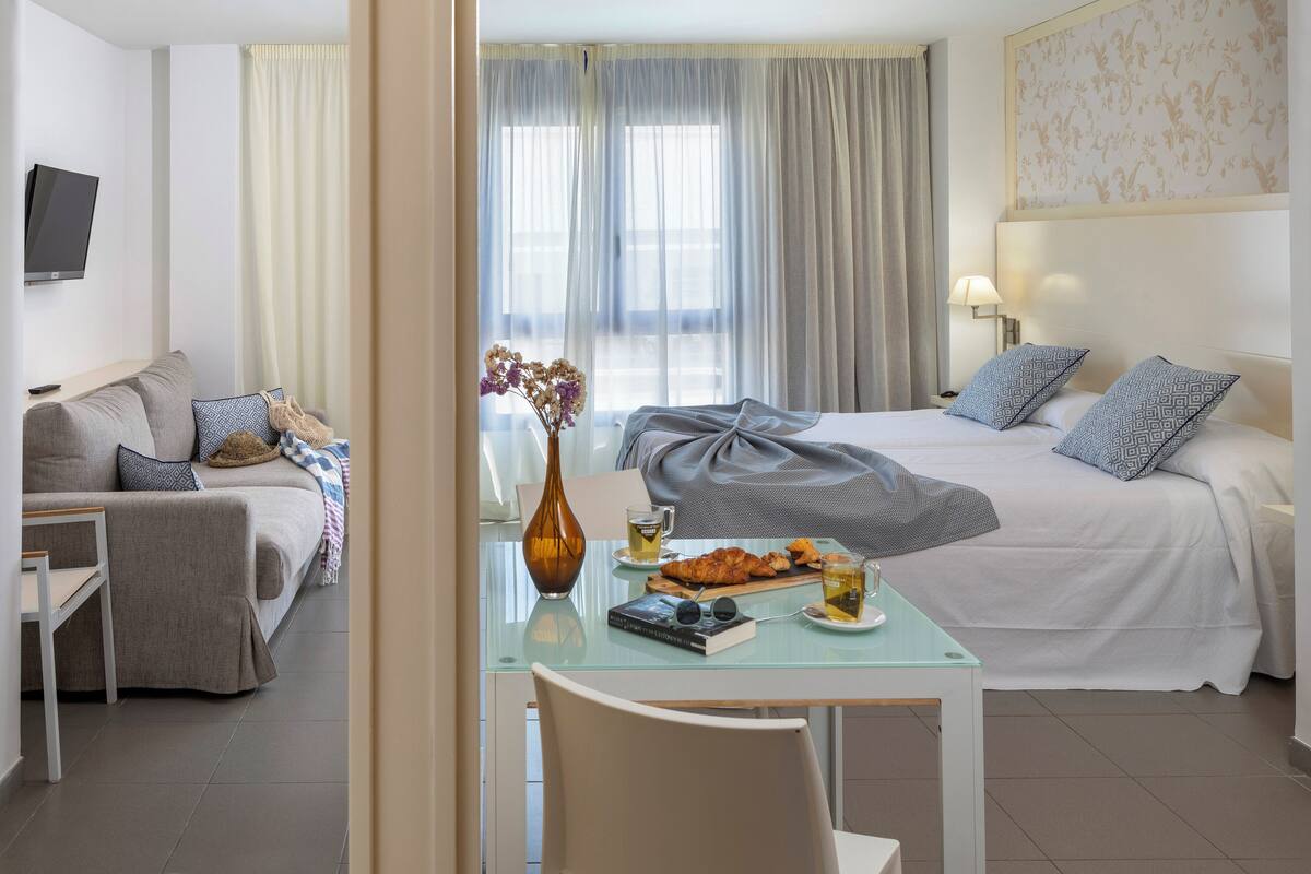 A hotel room with a bed, a sofa, a table with food and drinks, and a TV.