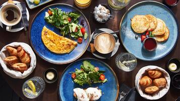 Una escena de desayuno con platos de comida, incluyendo huevos, tostadas y una ensalada, junto con bebidas y pasteles.