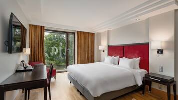 Habitación de hotel con una cama grande, un escritorio con silla, televisión y ventana con cortinas.