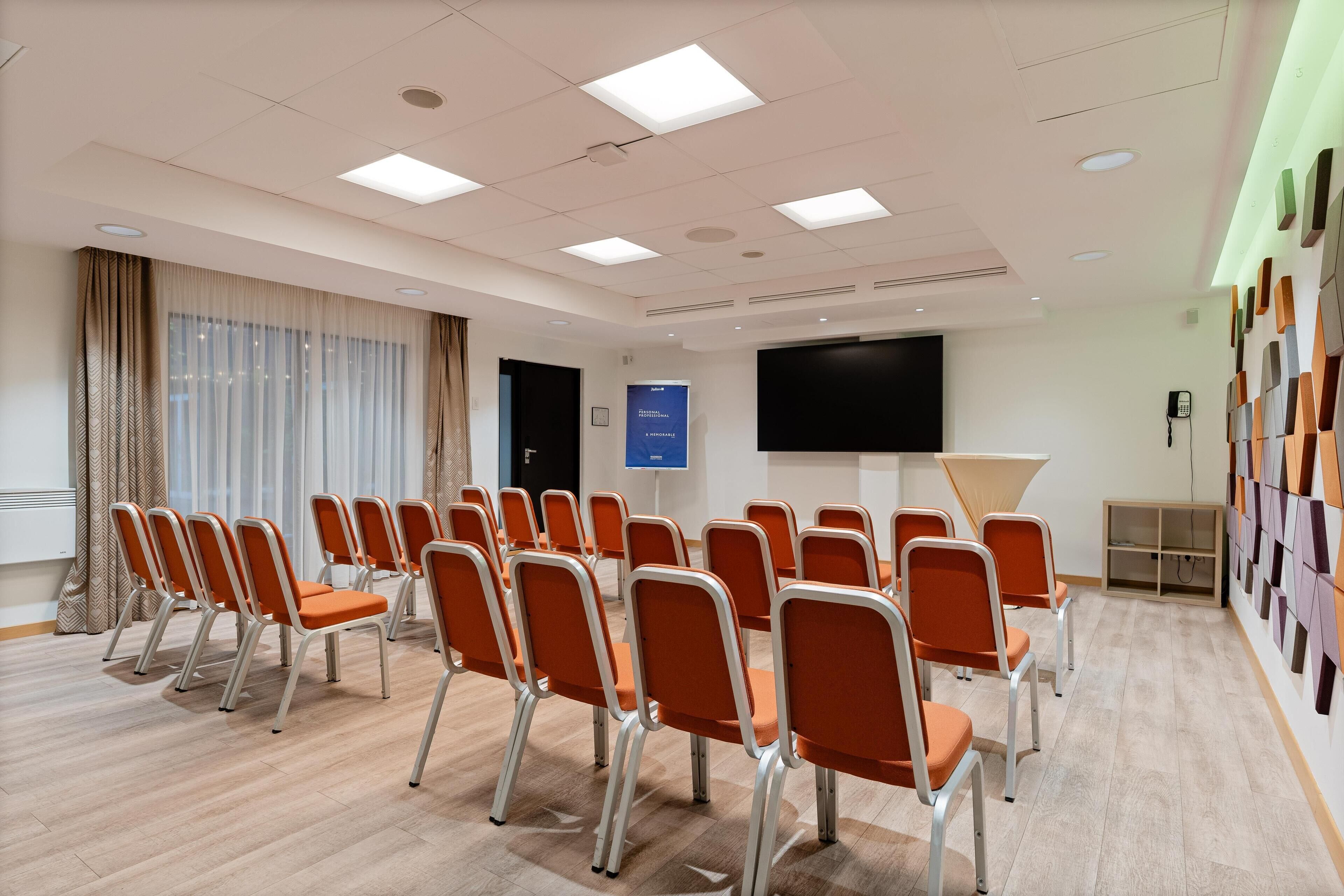 A conference room with rows of orange chairs, a large screen, and a projector.