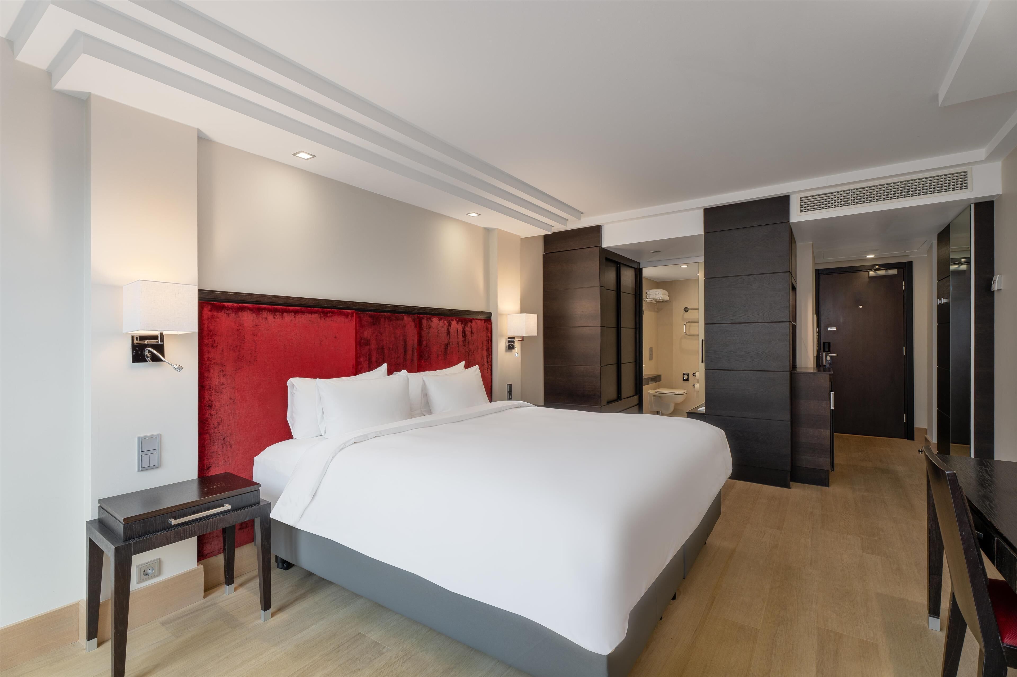 Una camera d'albergo moderna con un letto grande, una testiera rossa, un comodino e un armadio.