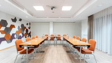 Un salón de conferencias con una mesa larga, sillas anaranjadas y un diseño geométrico en la pared.