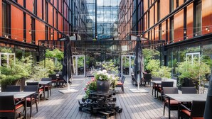 Un espace extérieur moderne, aménagé avec des tables et des chaises en bois, entouré de murs de verre et agrémenté de plantes en pot.