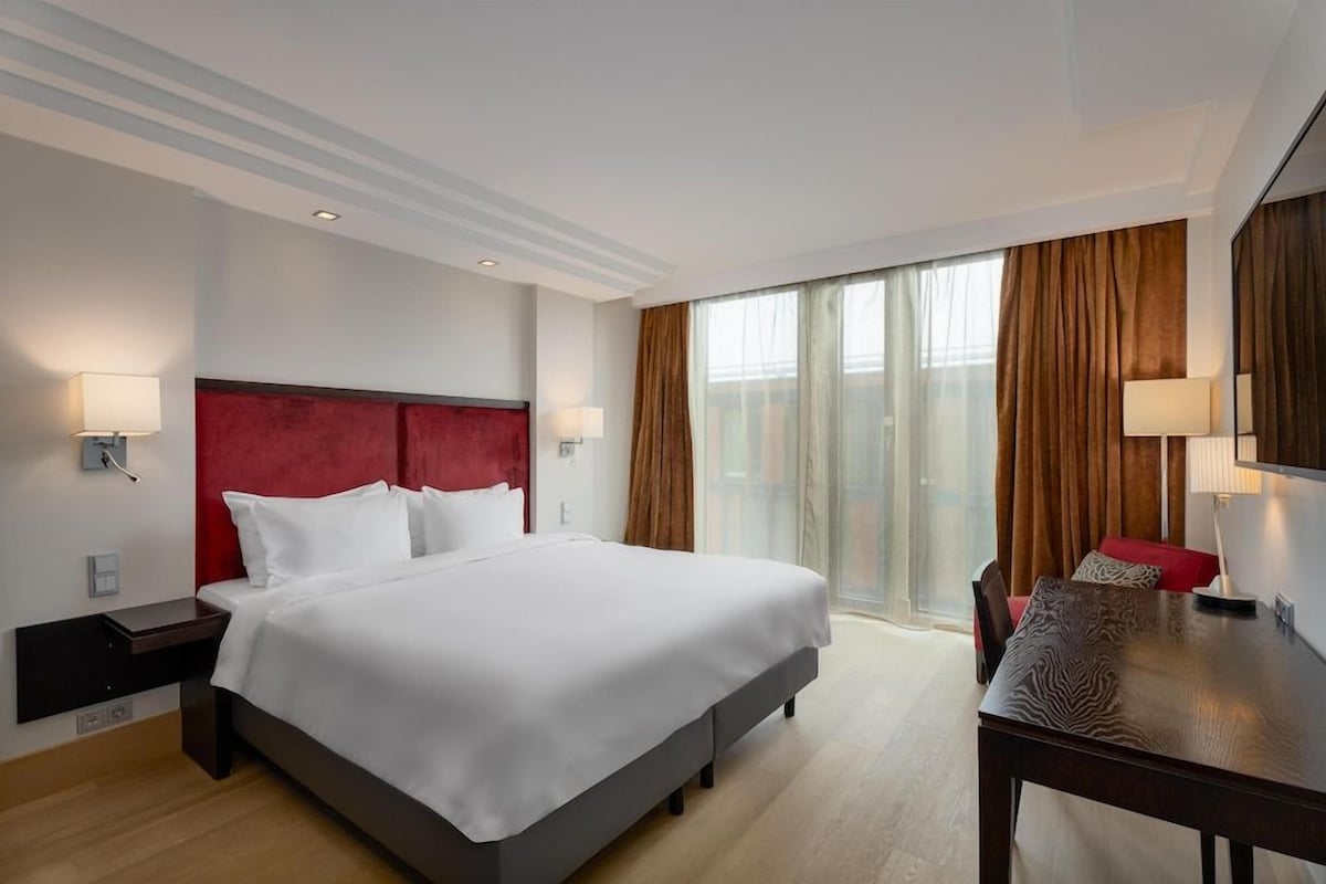 A hotel room with a large bed, a desk, and a view of the outdoors.