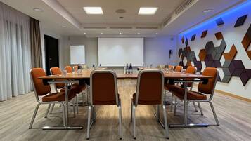 A conference room with a long table, orange chairs, a projector screen, and a wall with geometric patterns.