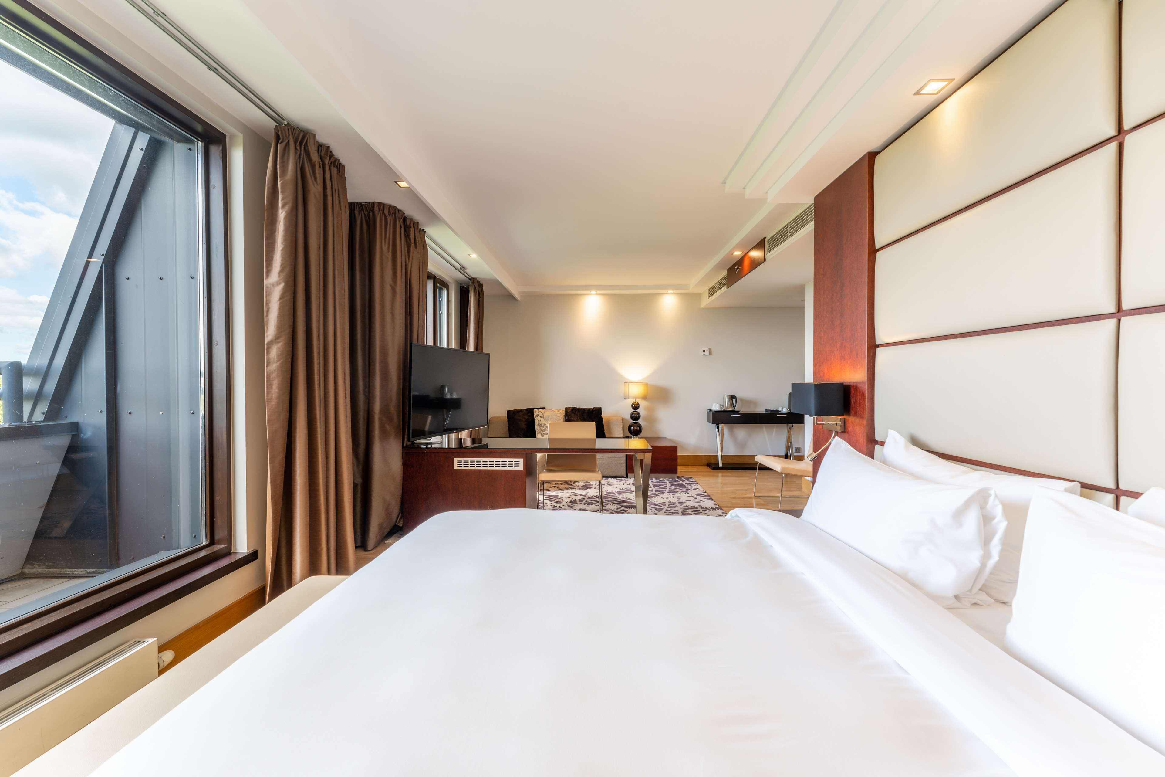 Habitación de hotel con una cama grande, un escritorio, una silla, un televisor y una ventana con cortinas.