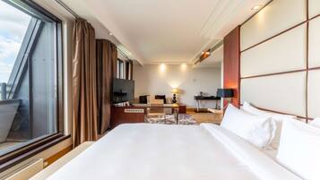 Habitación de hotel con una cama grande, un escritorio, una silla, un televisor y una ventana con cortinas.