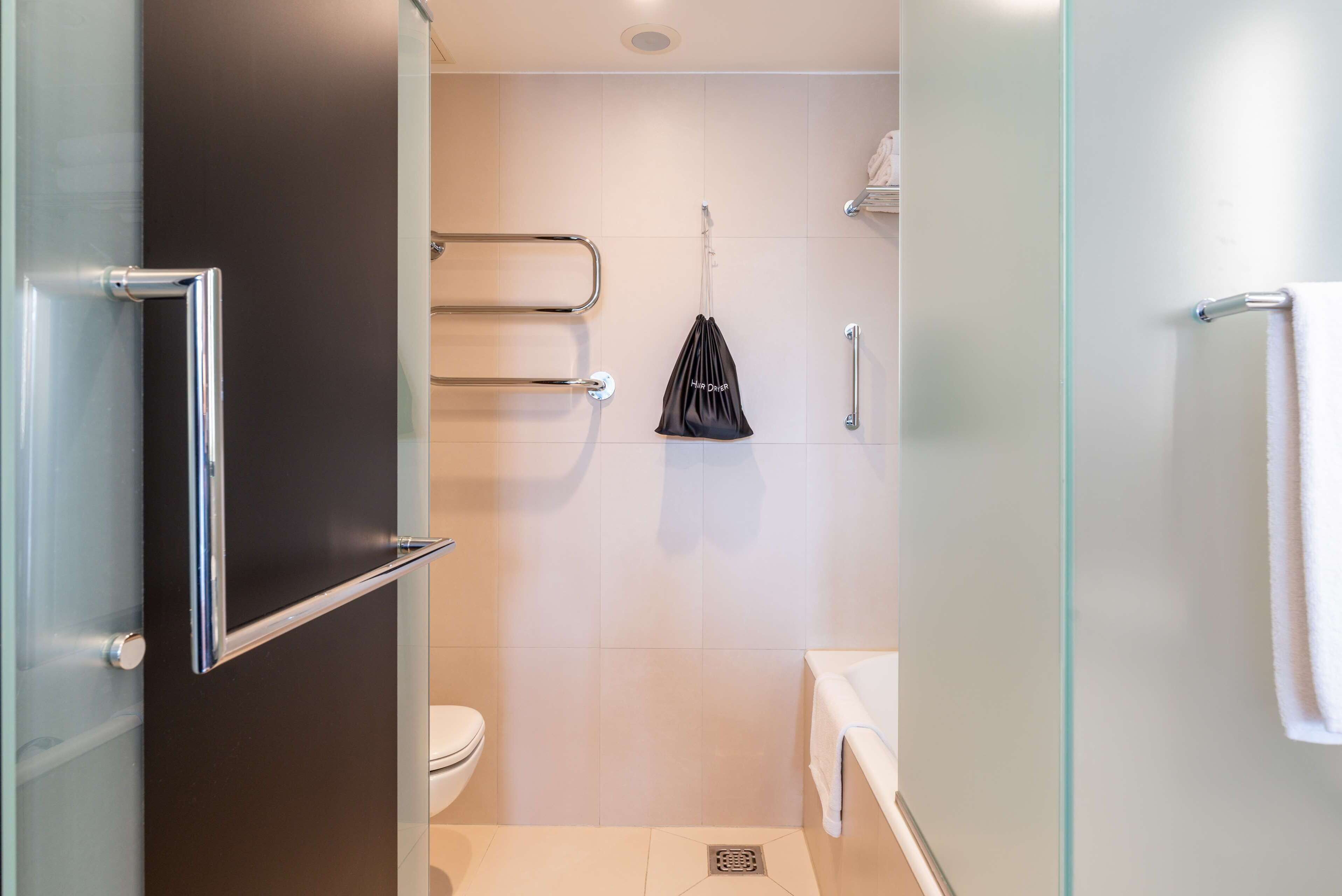 Un baño moderno con cabina de ducha de vidrio, inodoro y lavabo blancos, y una toalla colgada en la pared.