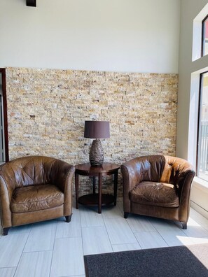 A room with two leather armchairs, a small round table with a lamp, and a stone wall. - Spanish Trails Inn (Mesquite)
