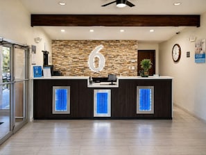 A reception desk with a stone wall backdrop, a clock, and a sign indicating the number 6. - Spanish Trails Inn (Mesquite)