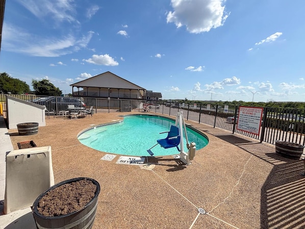 A swimming pool with a lifeguard chair, a covered seating area, and a fenced deck. - Spanish Trails Inn (Mesquite)