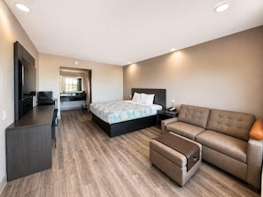 A modern hotel room with a bed, a sofa, a desk, and a TV. - Spanish Trails Inn (Mesquite)