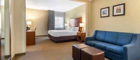 A hotel room with a bed, a blue sofa, a small table, a nightstand, and two framed pictures on the wall.