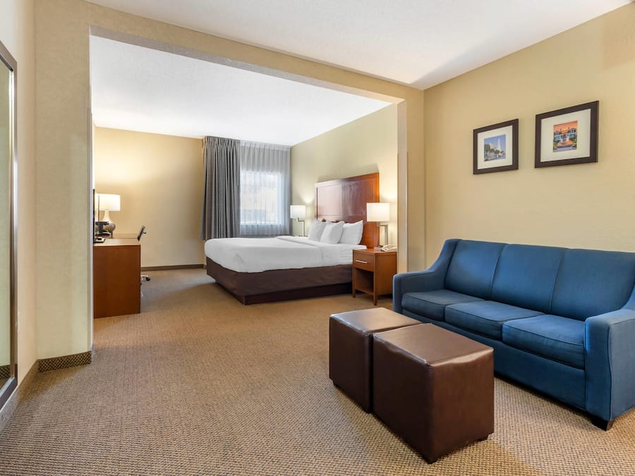 A hotel room with a bed, a blue sofa, a small table, a nightstand, and two framed pictures on the wall.