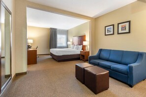 Ein Hotelzimmer mit Bett, blauem Sofa, kleinem Tisch, zwei Nachttischen und gerahmten Bildern an der Wand.