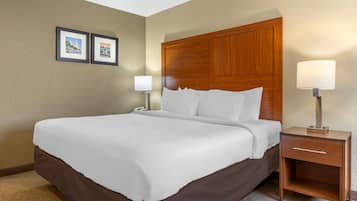 Una habitación de hotel con una cama grande, un cabecero de madera, dos lámparas de noche, una mesita de noche y dos cuadros en la pared.
