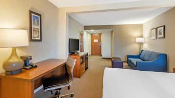 Una habitación de hotel con cama, escritorio, silla, televisor y sofá.