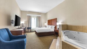 A hotel room with a bed, a desk with a TV, a chair, a bathroom with a bathtub, and a window with curtains. - Comfort Inn & Suites Sikeston I-55 (Sikeston)
