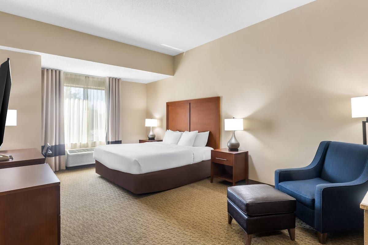 A hotel room with a large bed, a desk, a chair, and a small ottoman.