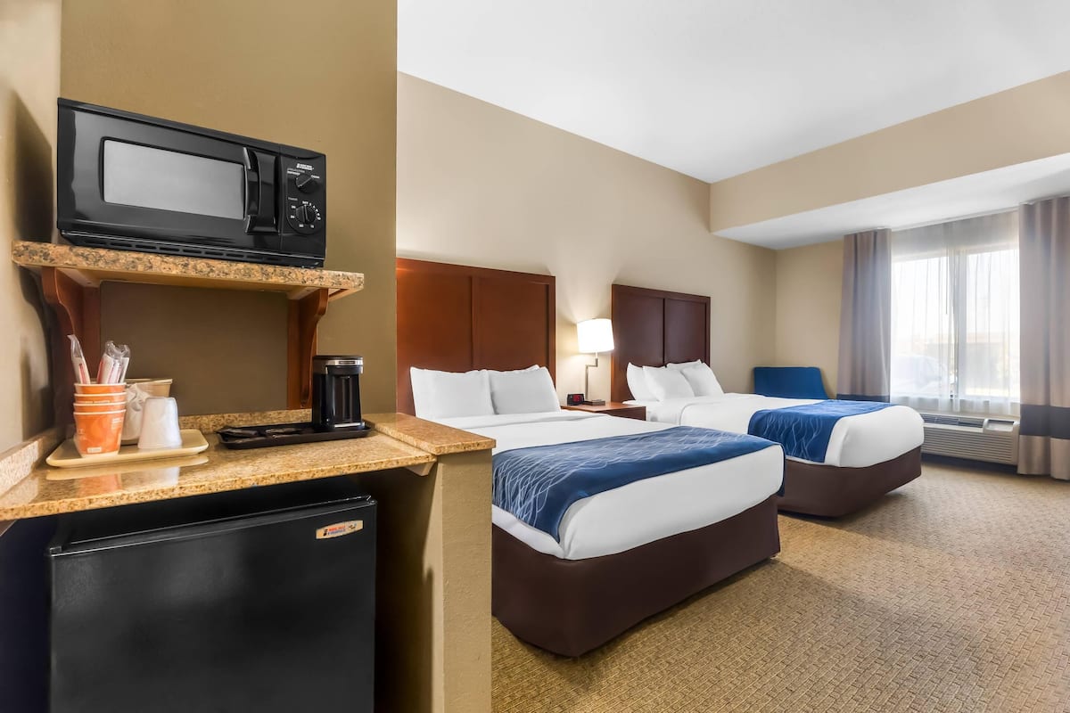A hotel room with two beds, a microwave, a mini-fridge, a coffee maker, and a window with curtains.