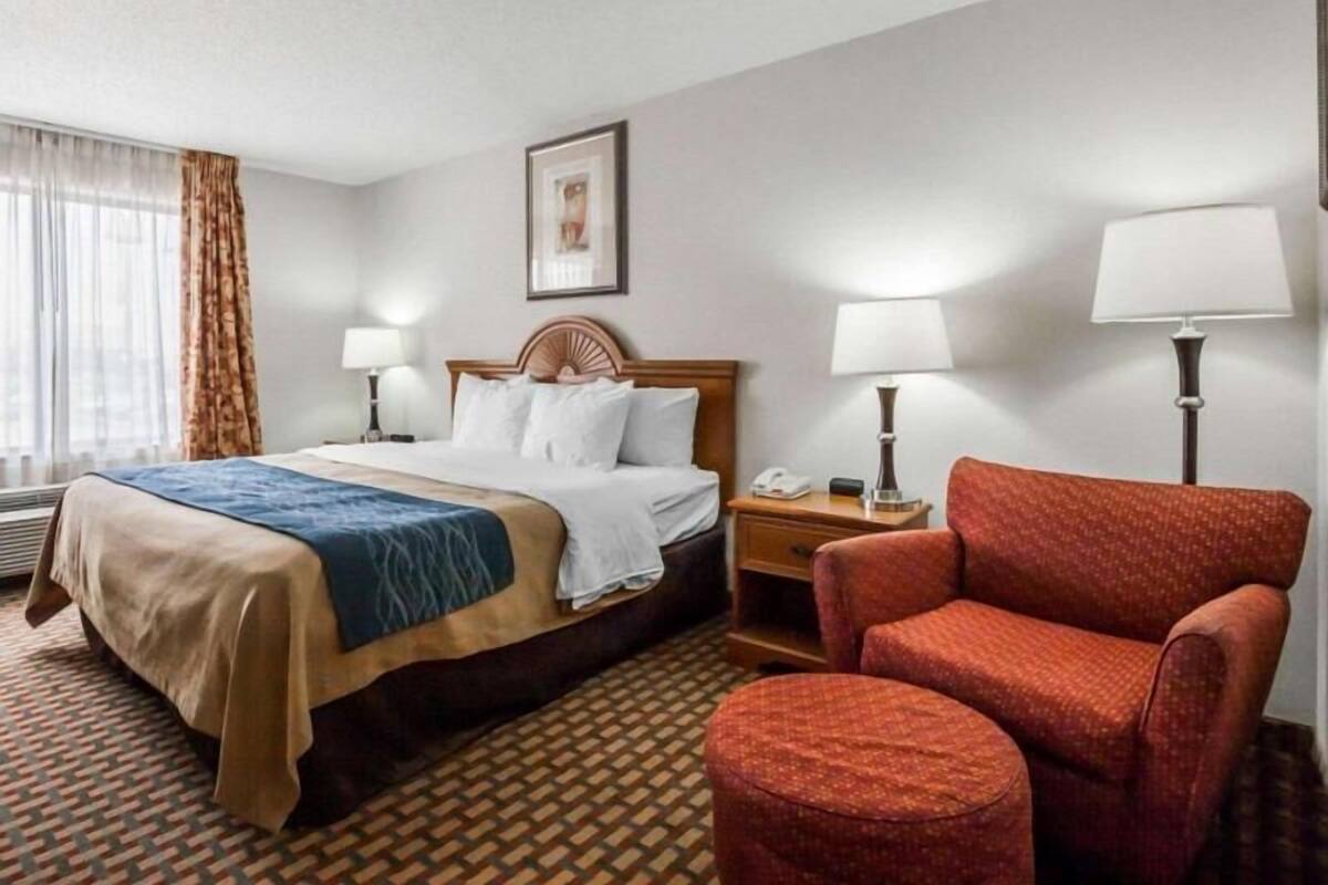A hotel room with a bed, two bedside tables with lamps, a chair, and a patterned carpet.
