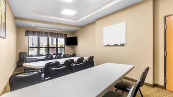 Una sala conferenze con un lungo tavolo, sedie, una lavagna e una TV appesa al muro.