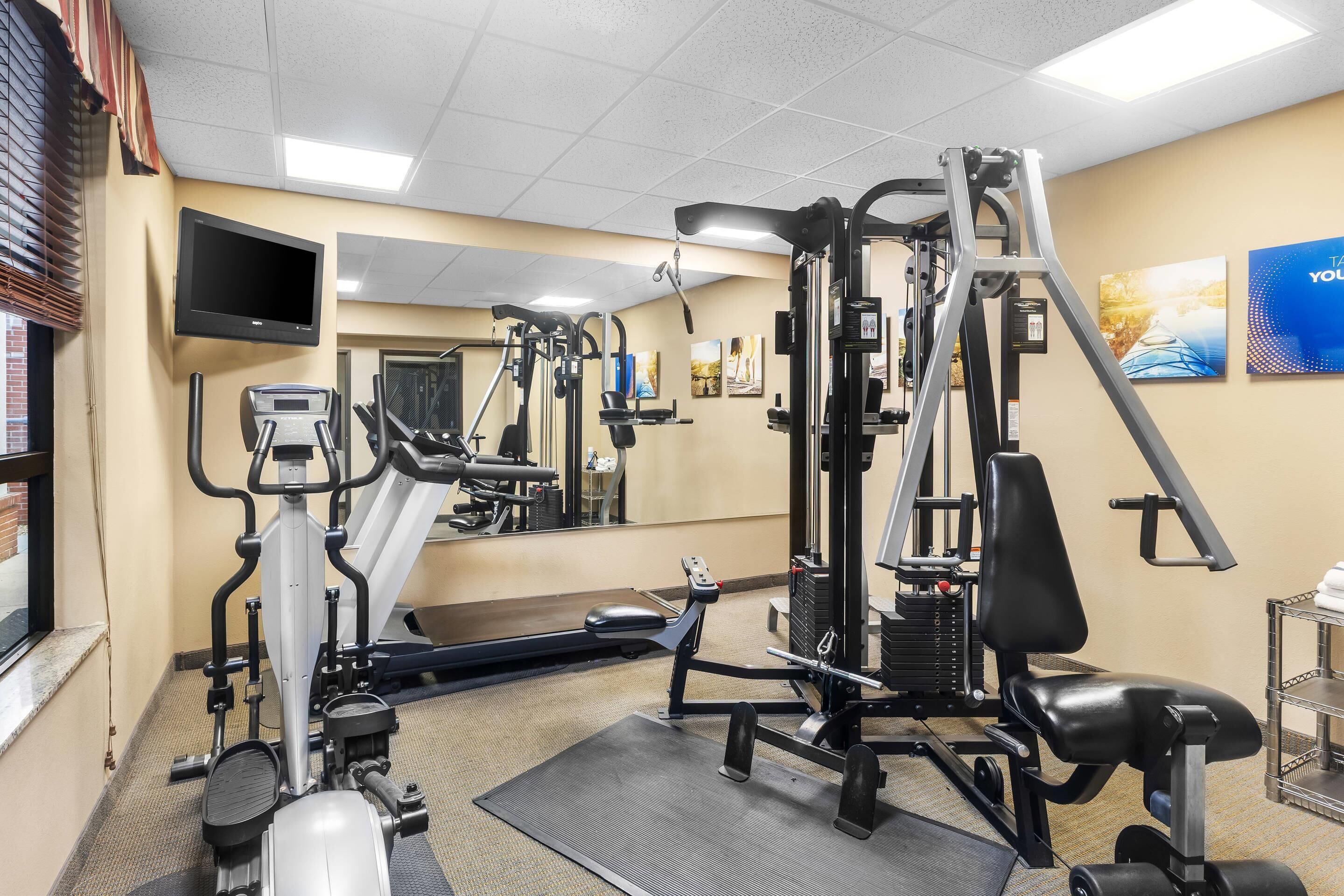 Een sportschool met diverse fitnessapparaten, een televisie en een spiegel aan de muur.