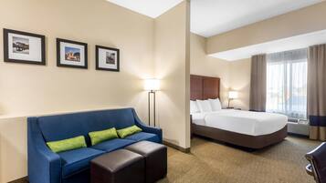 Habitación de hotel con un sofá azul, una cama, una mesita de noche y una lámpara. Hay tres cuadros enmarcados en la pared.